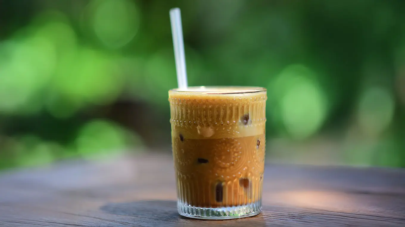 Cold Brew Kaffee mit strohhalm auf einem tisch vor grün