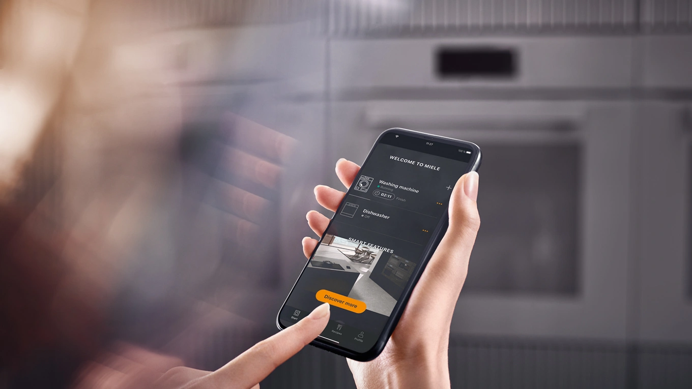 miele app für smarte küchengeräte auf einem smartphone dispay vor einem unscharfen miele backofen