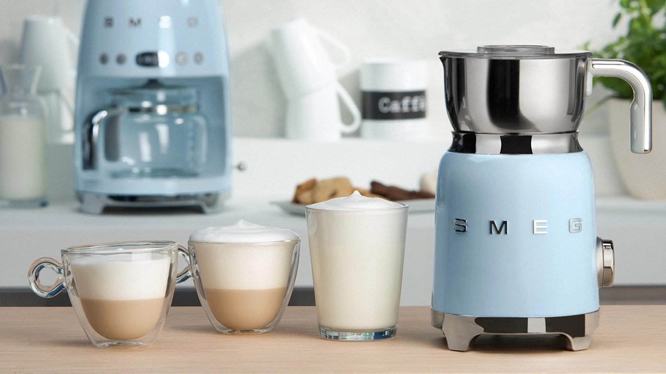smeg milchaufschäumer drei gläser mit unterschiedlich starkem milchschaum neben einem smeg milchaufschäumer in pastellblau