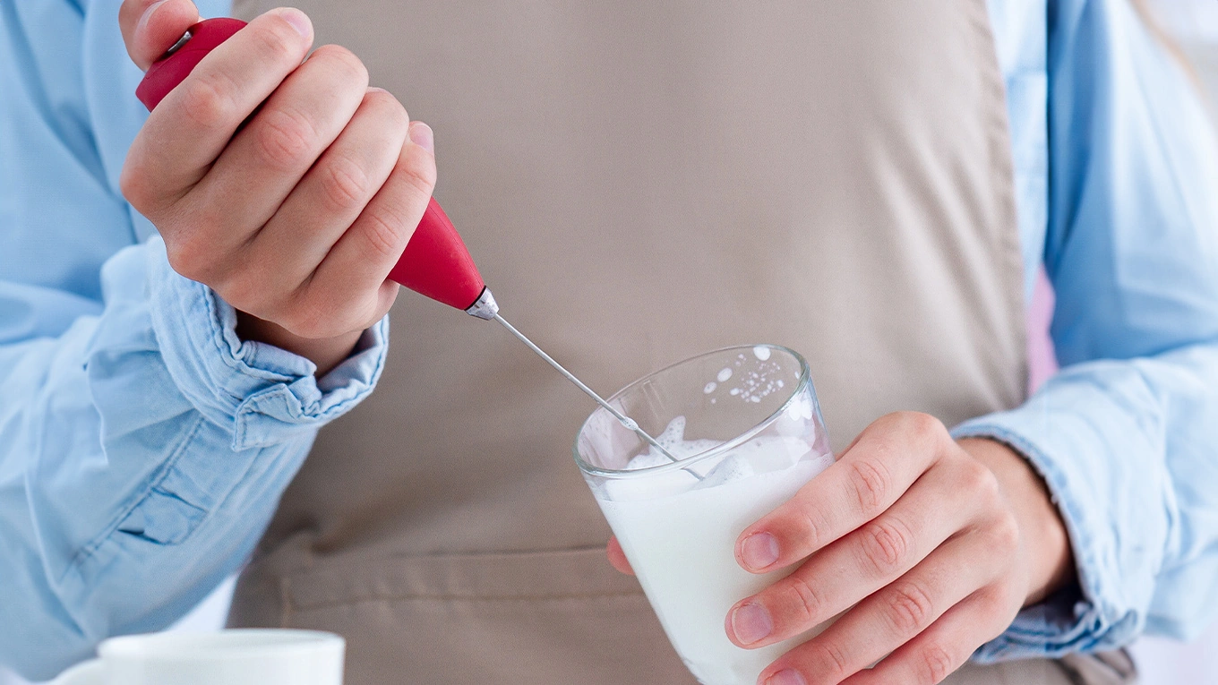 mann schlägt milch schaumig mit einem roten milchaufschäumer stab 