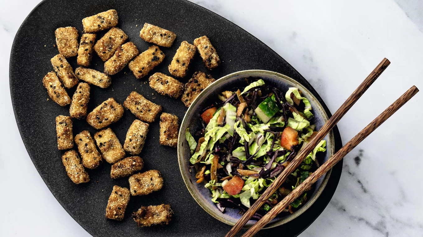 frittierter tofu neben einer schüssel salat auf einem schwarzen teller