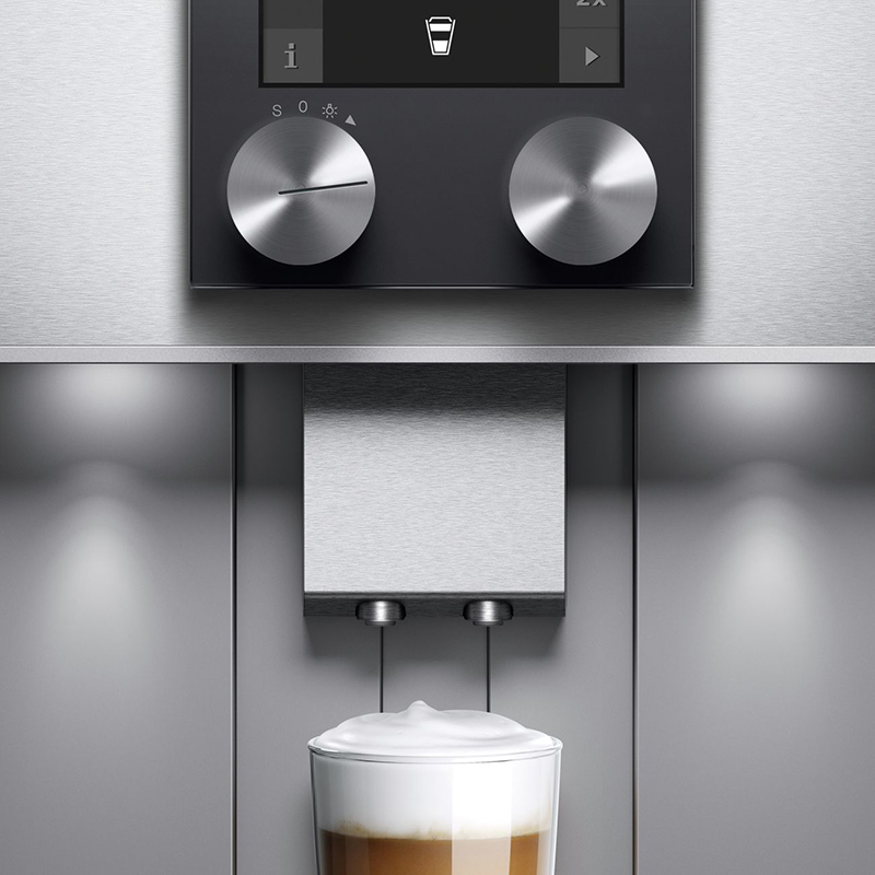 detailaufnahme von einem gaggenau kaffeevollautomat unter dem ein volles kaffeeglas mit milchschaum steht