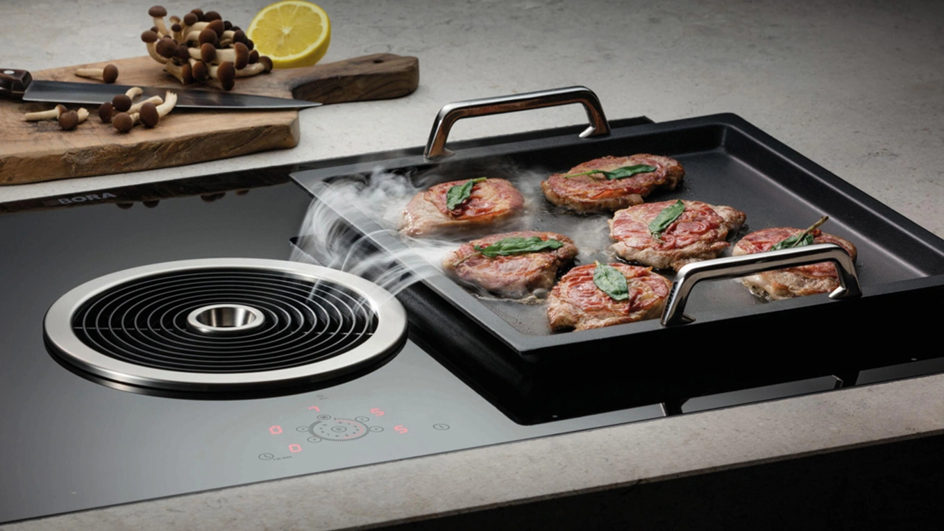 BORA Basic Kochfeld mit rundem Dunstabzug Bora basic Kochfeld mit runder einströmdüse die kochdunst vom fleisch auf einer danebeneliegenden grillplatte absaugt