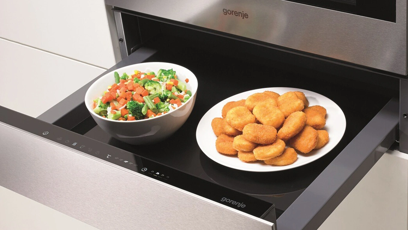 Teller mit Nuggets und Schüssel mit Gemüse in einer silbernen Wärmeschublade zum Warmhalten von Gorenje