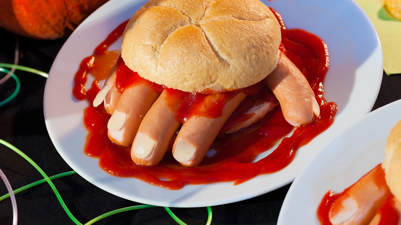 Würstchen Finger unter einem Burgerbrötchen mit viel Ketchup blut drumherum