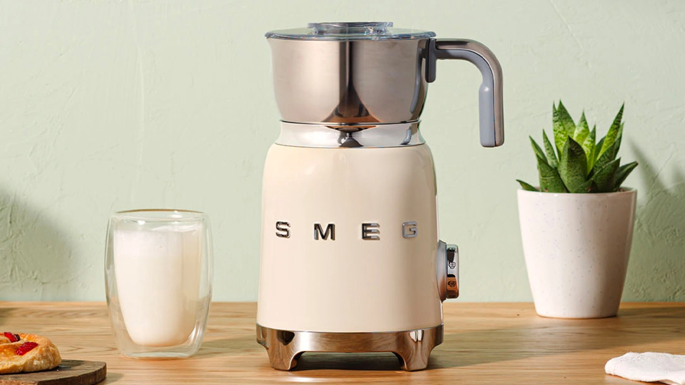 smeg milchaufschäumer in creme neben einer tasse voll mit cremigem milchschaum