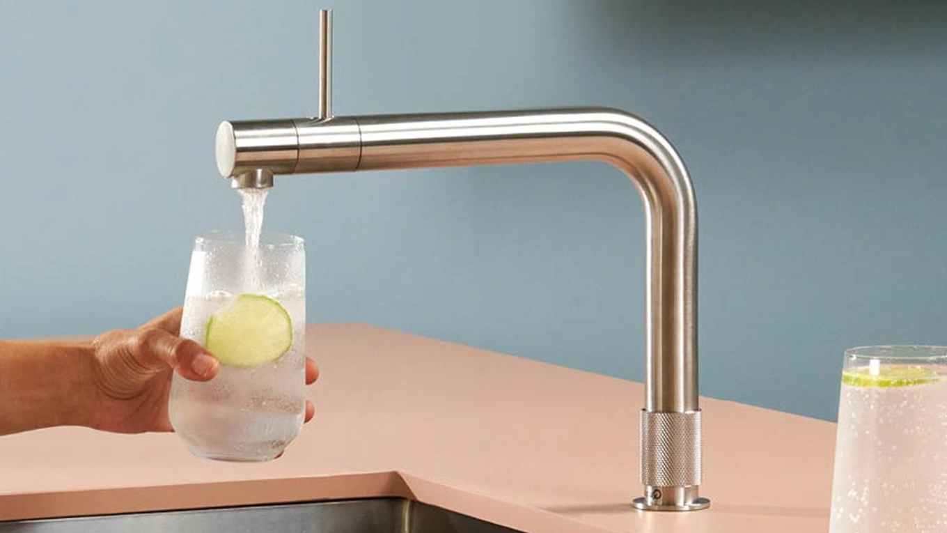 quooker front wasserhahn in edelstahl befüllt ein glas mit limettenscheibe mit kaltem sprudelwasser