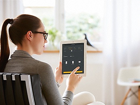 Frau mit Pferdeschwanz und Brille, die ein Tablet mit Miele At Home App auf dem Display hält